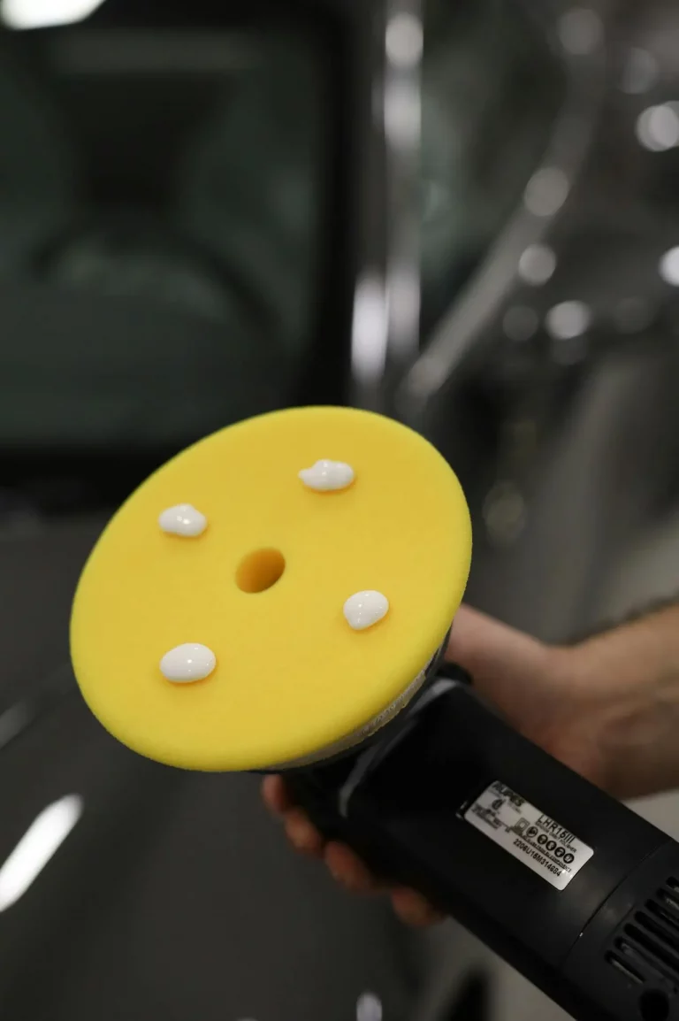 Poliermaschine mit gelbem Polierpad und Autopolitur vor dem Polieren eines Fahrzeugs